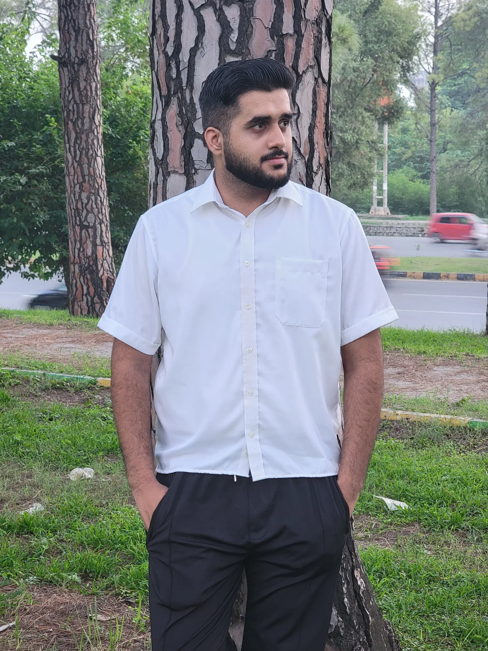 Ahmed standing among trees in a white shirt