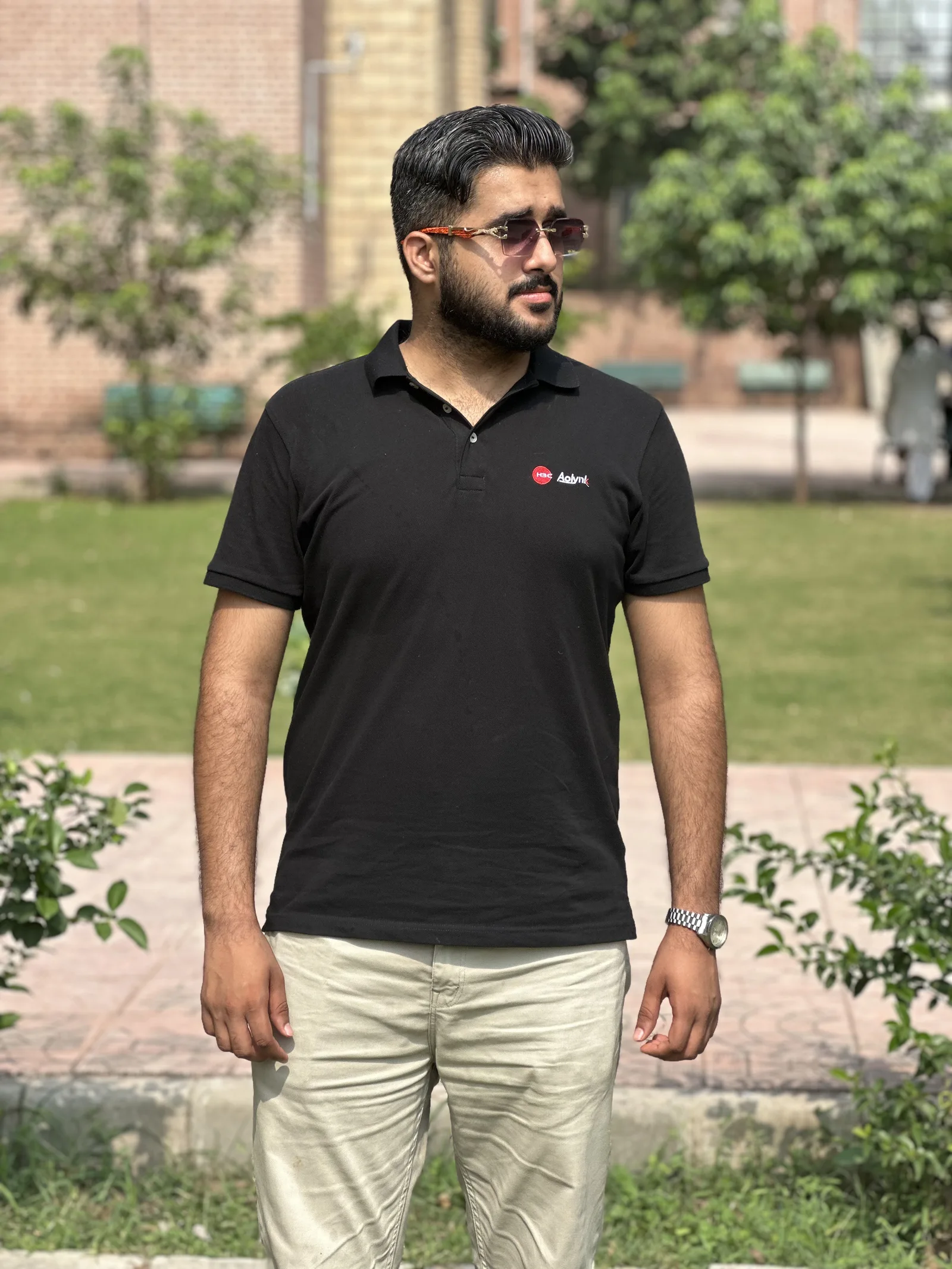 Ahmed Ali outdoors, wearing a black polo shirt and sunglasses